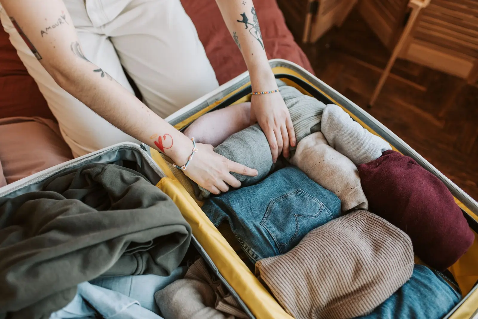 Person packt Kleidung übersichtlich in einen geöffneten Reisekoffer